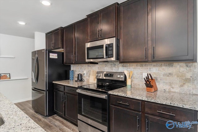 kitchen with stainless steel appliances, tasteful backsplash, light stone counters, light hardwood / wood-style flooring, and dark brown cabinets