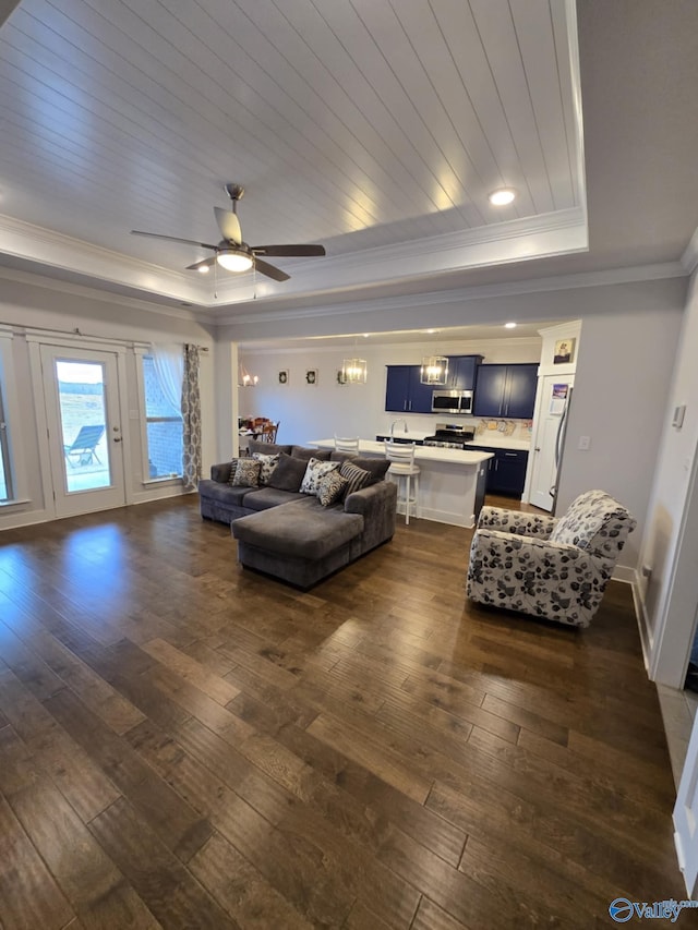 living area with dark wood-style floors, a tray ceiling, ornamental molding, wooden ceiling, and ceiling fan with notable chandelier