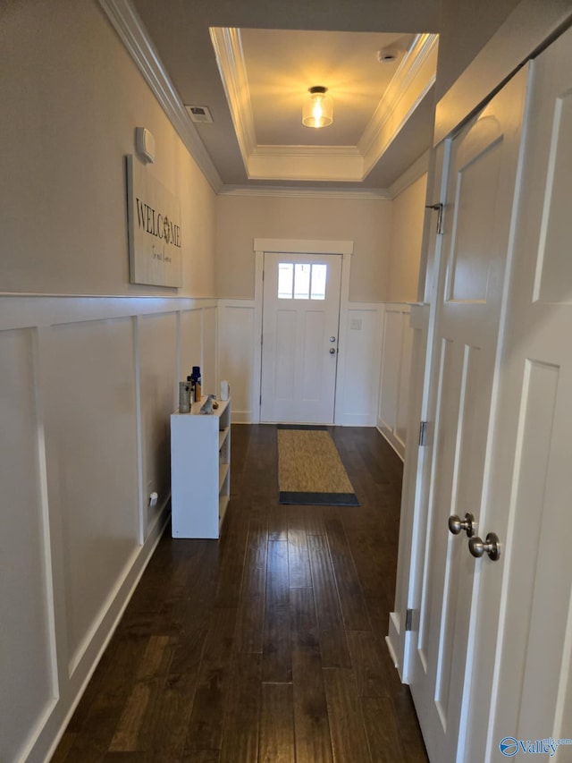 doorway with visible vents, dark wood-type flooring, ornamental molding, wainscoting, and a raised ceiling