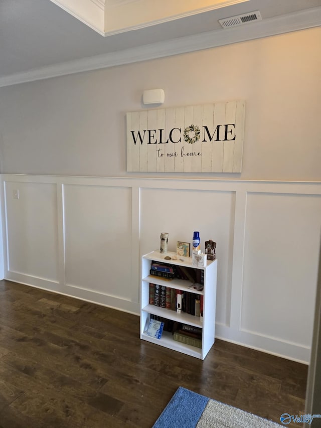 room details with visible vents, crown molding, a decorative wall, and wood finished floors