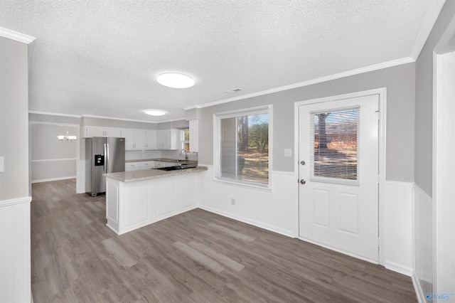 kitchen featuring stainless steel refrigerator with ice dispenser, white cabinetry, crown molding, kitchen peninsula, and hardwood / wood-style flooring