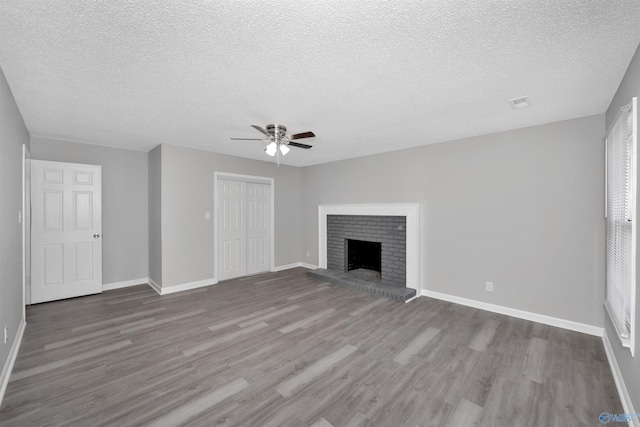 unfurnished living room featuring ceiling fan, wood-type flooring, a brick fireplace, and a textured ceiling