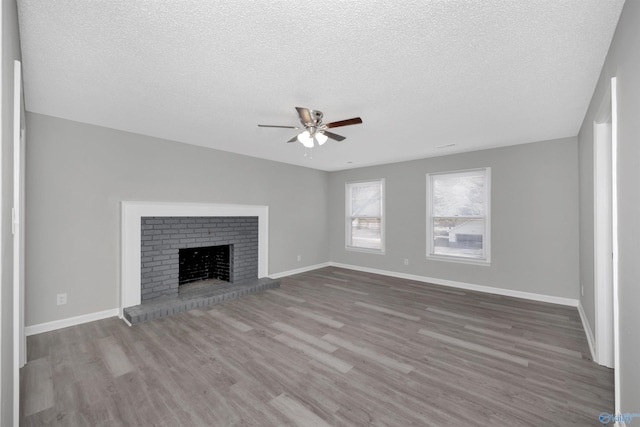 unfurnished living room with wood-type flooring, a brick fireplace, ceiling fan, and a textured ceiling