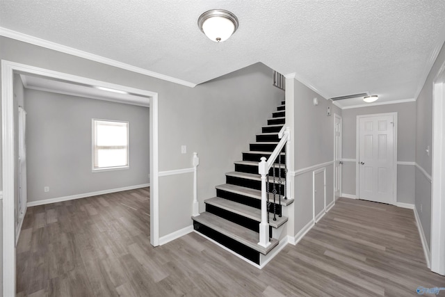 stairway with crown molding, hardwood / wood-style floors, and a textured ceiling