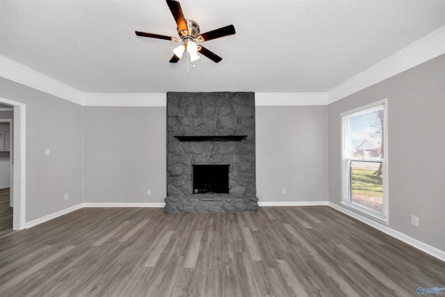 unfurnished living room with hardwood / wood-style flooring, crown molding, a stone fireplace, and a textured ceiling