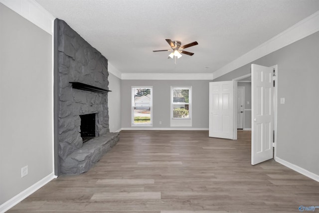 unfurnished living room featuring ceiling fan, a stone fireplace, a textured ceiling, and light wood-type flooring