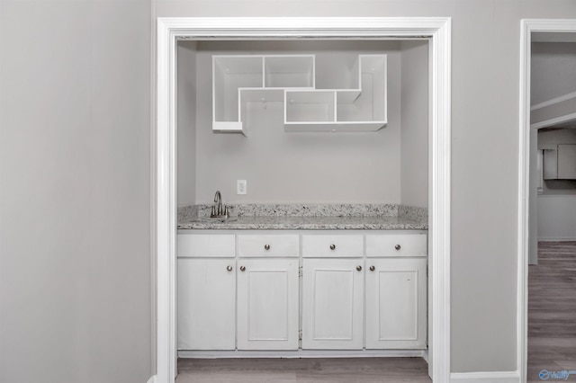 bar with white cabinetry, light stone countertops, sink, and light hardwood / wood-style flooring