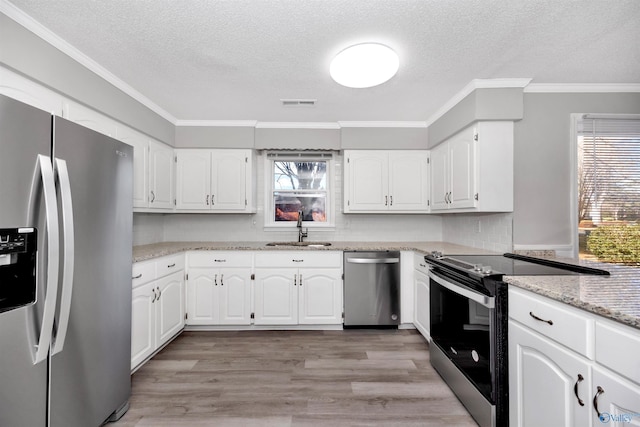 kitchen featuring appliances with stainless steel finishes, sink, white cabinets, ornamental molding, and light wood-type flooring