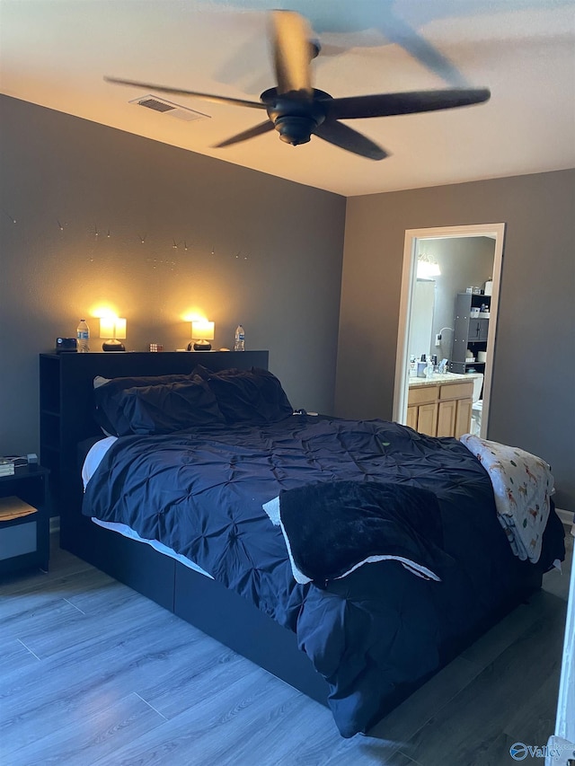 bedroom featuring wood finished floors, ensuite bathroom, ceiling fan, and visible vents