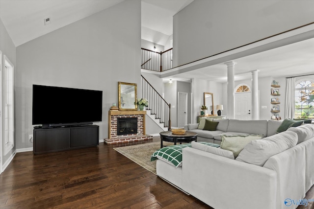 living room featuring dark hardwood / wood-style flooring, a brick fireplace, high vaulted ceiling, and ornate columns