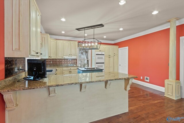 kitchen with double oven, cream cabinets, a peninsula, and decorative columns