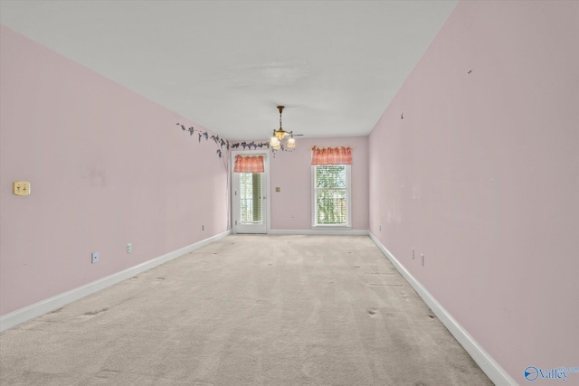 spare room with a chandelier, light carpet, and baseboards