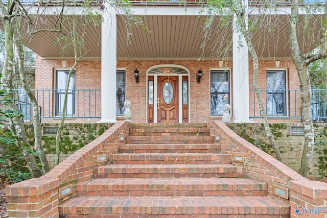 view of exterior entry featuring a porch and brick siding