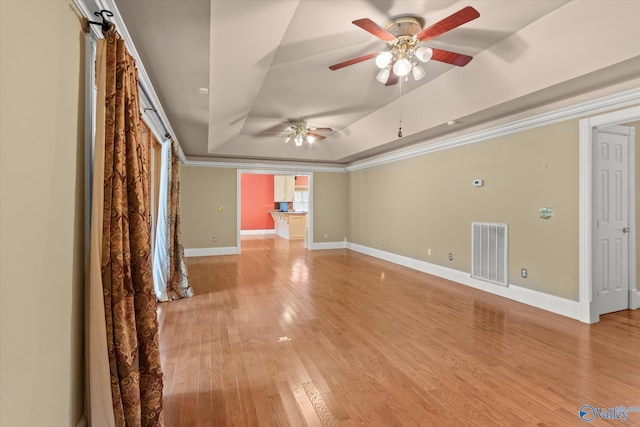 unfurnished living room with visible vents, a raised ceiling, baseboards, light wood-style flooring, and ornamental molding