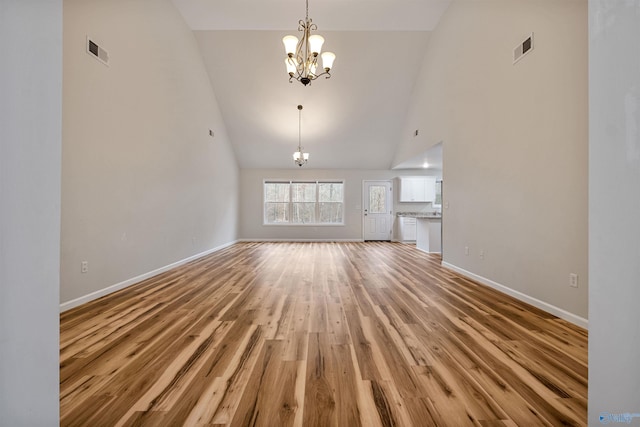 unfurnished living room featuring a notable chandelier, light hardwood / wood-style flooring, and high vaulted ceiling