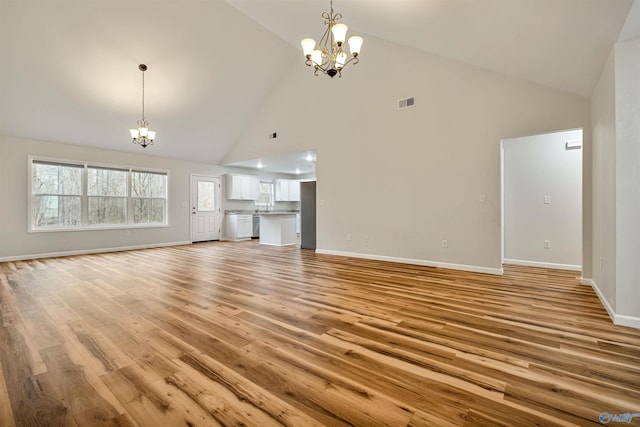 unfurnished living room featuring high vaulted ceiling, light wood-type flooring, and a notable chandelier