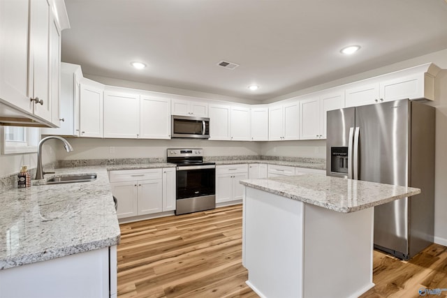 kitchen with sink, white cabinetry, stainless steel appliances, light stone counters, and a kitchen island