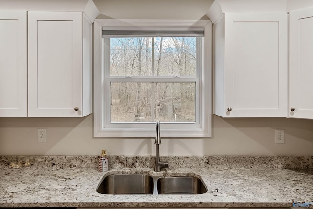 kitchen featuring light stone countertops, sink, and white cabinets