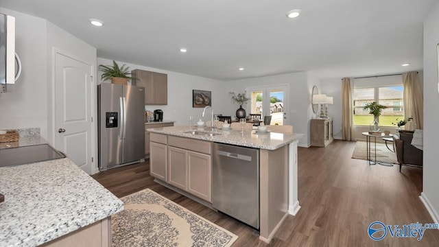 kitchen featuring sink, light stone counters, dark hardwood / wood-style floors, a kitchen island with sink, and appliances with stainless steel finishes