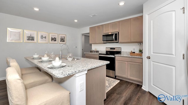 kitchen with a kitchen bar, dark wood-type flooring, sink, appliances with stainless steel finishes, and light stone counters