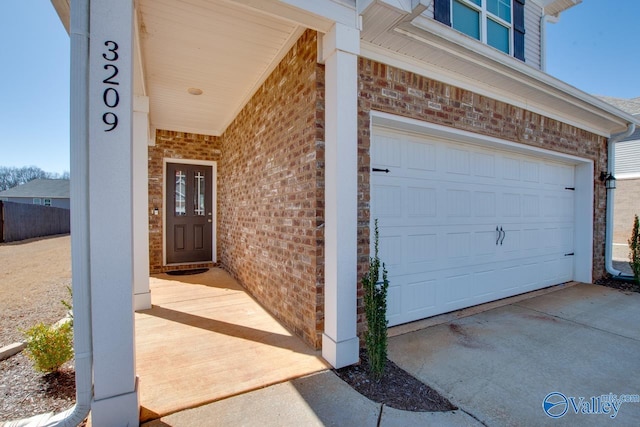 doorway to property with a garage, brick siding, and concrete driveway