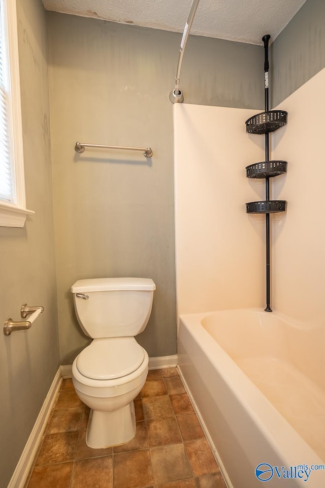 full bathroom featuring toilet, baseboards, and a textured ceiling