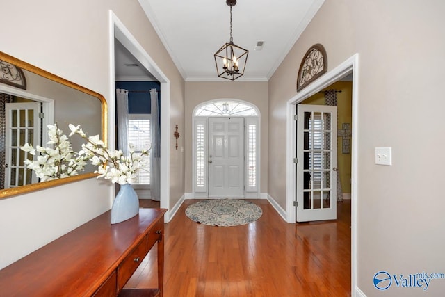 foyer entrance with a notable chandelier, crown molding, baseboards, and wood finished floors