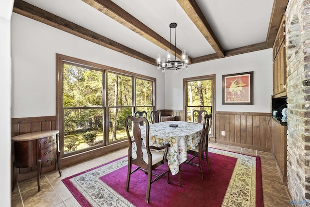 dining area featuring beamed ceiling, a notable chandelier, a healthy amount of sunlight, and wood walls