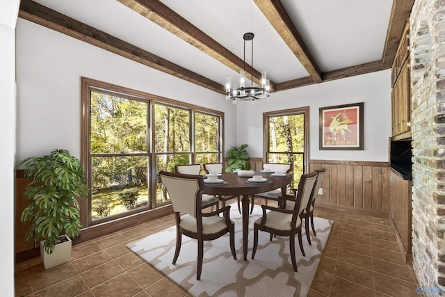 tiled dining room with an inviting chandelier, beam ceiling, wooden walls, and plenty of natural light