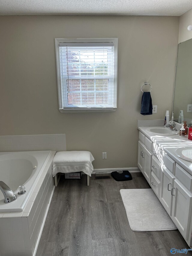 bathroom with hardwood / wood-style floors, vanity, a textured ceiling, and tiled tub