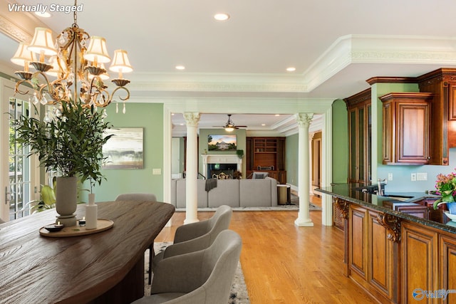 dining space featuring light wood-type flooring, crown molding, ceiling fan with notable chandelier, and ornate columns