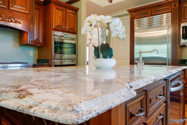 kitchen featuring a center island with sink, light stone counters, crown molding, and built in appliances