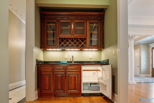 bar with sink, decorative columns, light hardwood / wood-style flooring, and ornamental molding