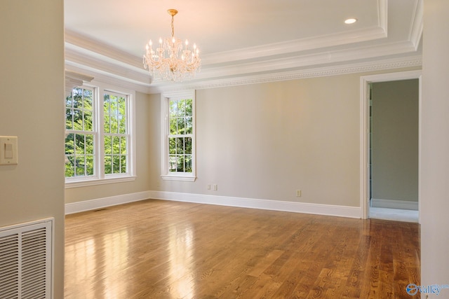 spare room with a raised ceiling, crown molding, wood-type flooring, and a chandelier