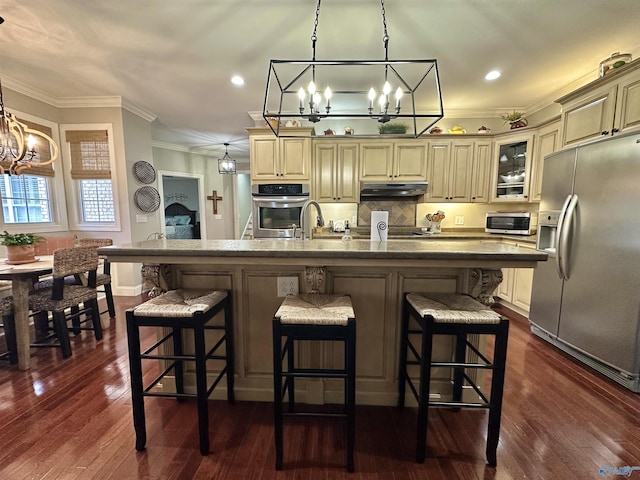 kitchen with stainless steel appliances, a kitchen breakfast bar, cream cabinets, an island with sink, and decorative light fixtures