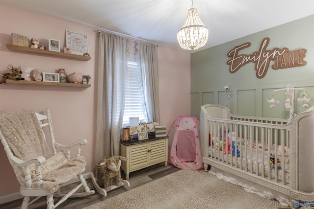 bedroom with a nursery area, dark wood-type flooring, and an inviting chandelier