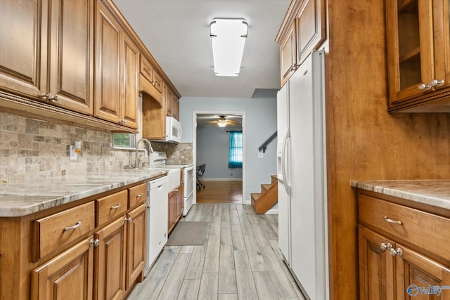 kitchen featuring brown cabinets, backsplash, glass insert cabinets, light stone countertops, and white appliances