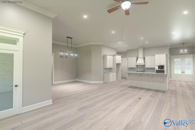 kitchen featuring pendant lighting, built in microwave, white cabinetry, an island with sink, and custom range hood