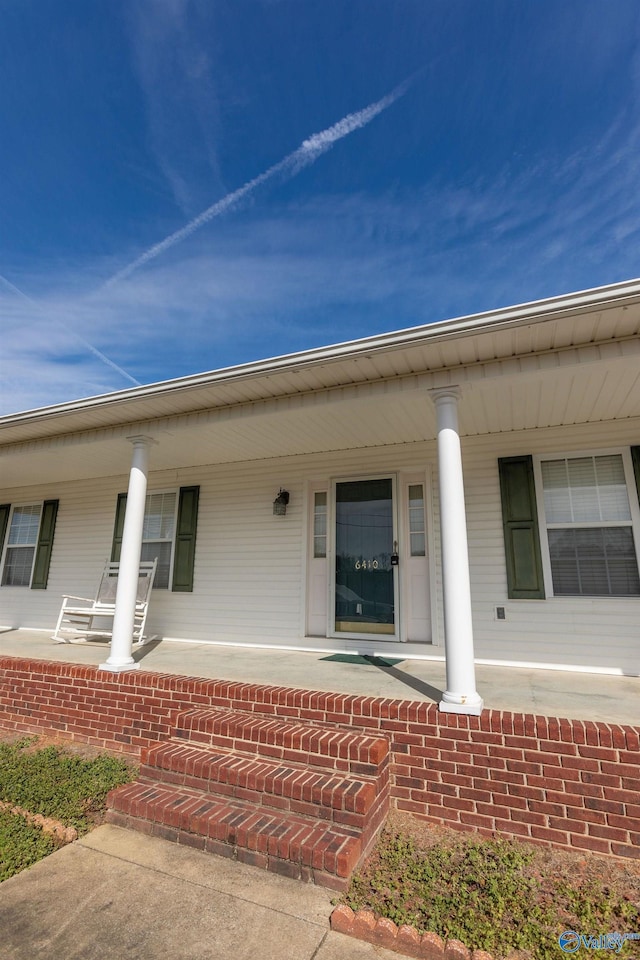 view of exterior entry featuring a porch and brick siding