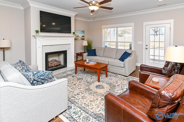 living room featuring visible vents, wood finished floors, a fireplace, crown molding, and ceiling fan