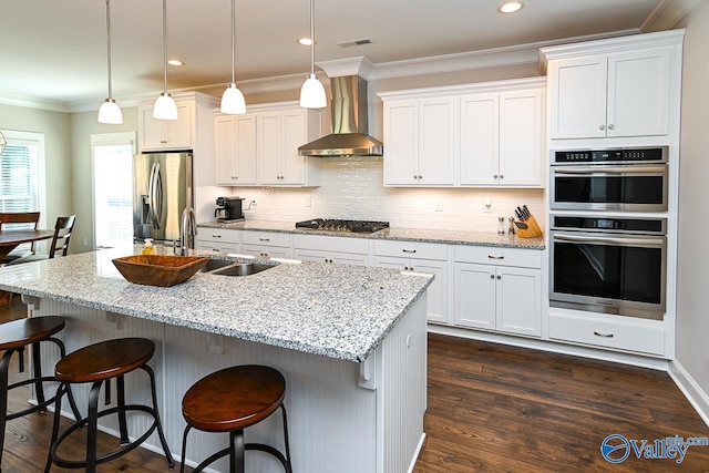 kitchen with dark wood-type flooring, wall chimney range hood, ornamental molding, stainless steel appliances, and a sink