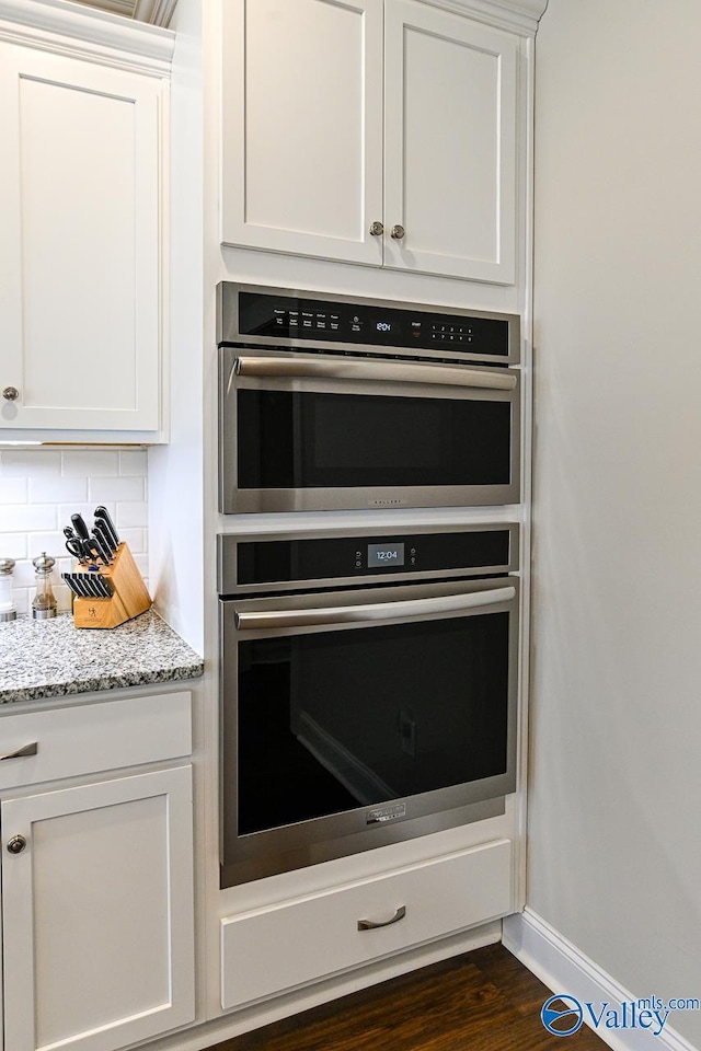 interior details with backsplash, baseboards, light stone countertops, double oven, and white cabinets