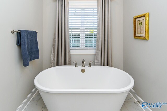 full bath featuring a freestanding tub, baseboards, and marble finish floor