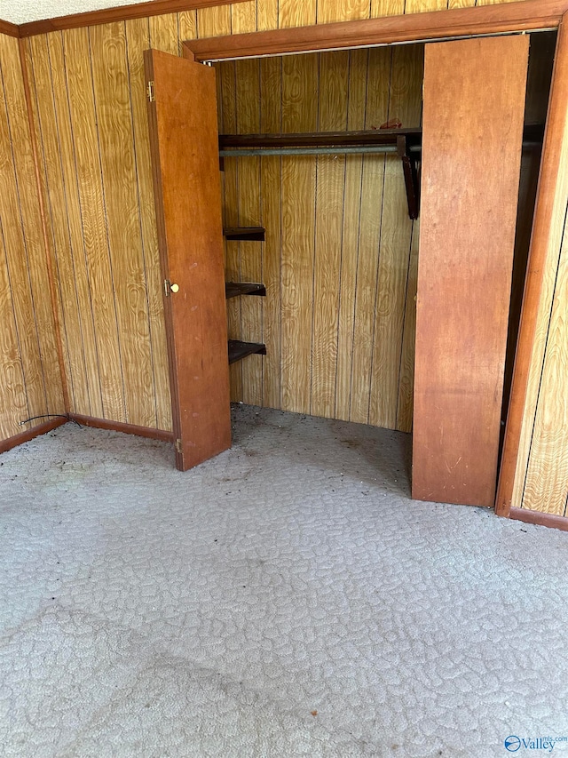 unfurnished bedroom featuring a closet, wood walls, and light colored carpet