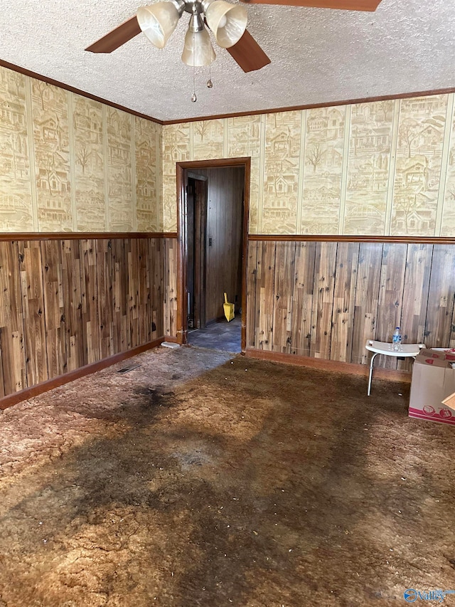 empty room with ceiling fan, a textured ceiling, and wooden walls