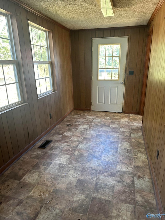 doorway with a healthy amount of sunlight, a textured ceiling, and wooden walls