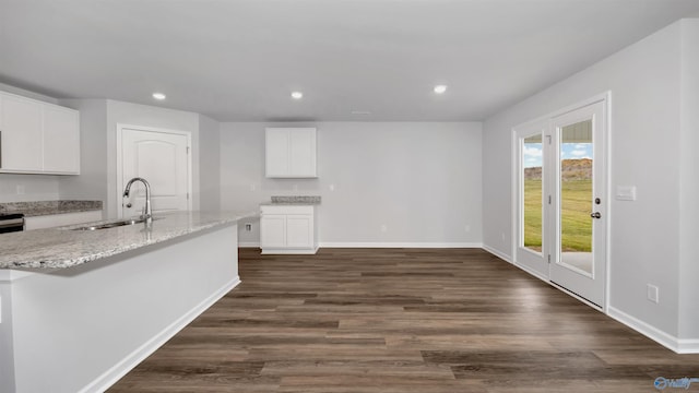 kitchen featuring white cabinetry, sink, light stone countertops, dark wood-type flooring, and a center island with sink