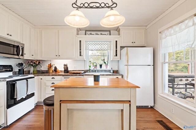 kitchen with light wood finished floors, stainless steel microwave, electric range oven, freestanding refrigerator, and a kitchen island