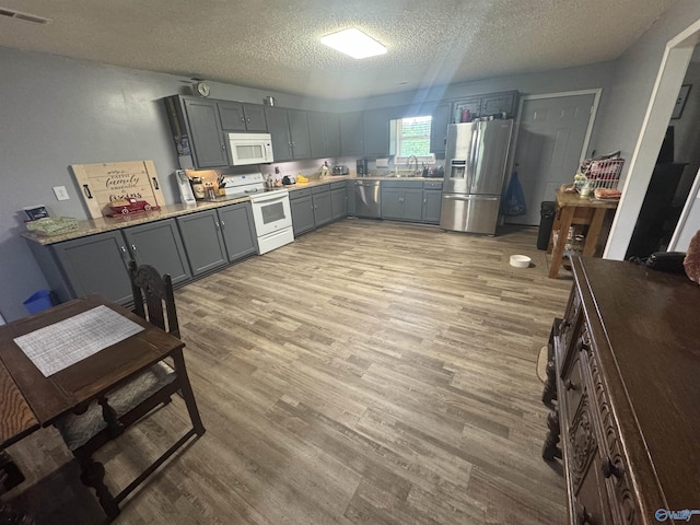 kitchen featuring gray cabinetry, a textured ceiling, visible vents, light wood-style floors, and stainless steel appliances