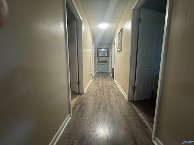 corridor with dark wood finished floors, baseboards, and a textured ceiling